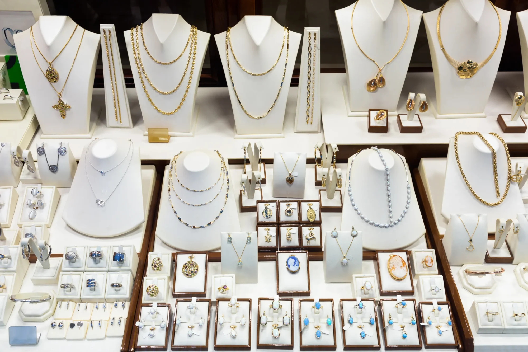 A display case filled with various gold and silver necklaces, rings, bracelets, earrings, and pendants, each arranged neatly on white stands and trays in a jewelry store.