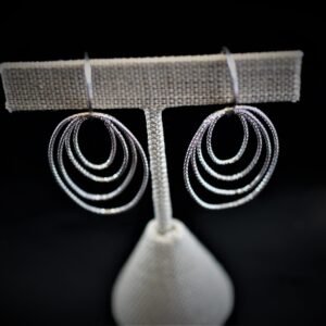 Radiant Hoop Earrings in Sterling Silver, featuring multi-hoop dangling movement and shine, displayed on a beige textured T-shaped stand against a black background.
