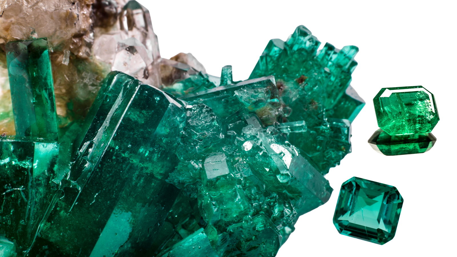 Cluster of vivid green emerald crystals with sharp edges and transparent facets, alongside two cut and polished emerald gemstones, all set against a white background.